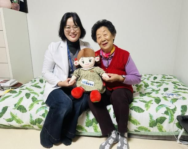 화성시동탄보건소 관계자와 독거 어르신이 AI 돌봄로봇 ‘효돌이’를 함께 들고 환하게 웃고 있다